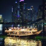 A traditional dhow boat illuminated against the stunning night skyline of Dubai Marina.